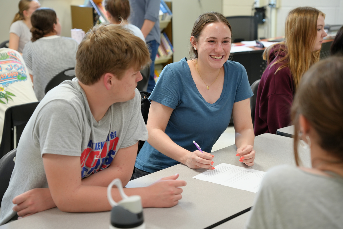 student smiles while working on a worksheet with her classmates surrounding her